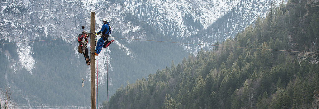 Techniker arbeitet auf Strommast in alpiner Landschaft nahe See